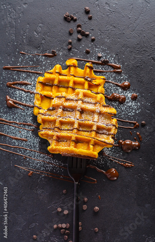 Pumpkin waffles with chocolate and sugar powder strung on forkon dark old background. Top view photo