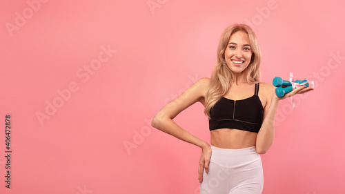 Gorgeous sporty blonde woman holding dumbbells with gift ribbon over pink background, banner design with copy space © Prostock-studio