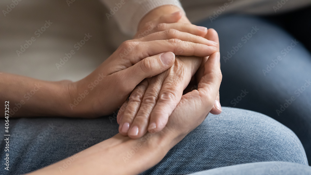 Close up caring grown up daughter touching mature mother hand, comforting and calming, expressing love and support, young woman and elderly mum holding hands, two generations trusted relations