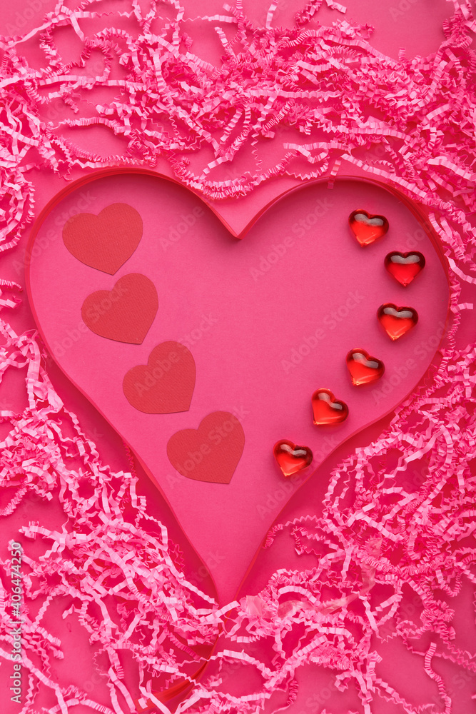 On a pink background, Valentine's Day decoration of a volumetric heart made of paper and pebbles and ribbons.