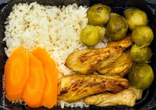 Slices of fried chicken chicken with boiled broccoli  carrots and rice close-up on a black plastic backing