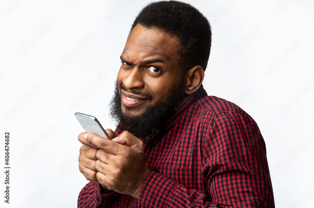 Suspicious Black Man Using Smartphone Looking At Camera, White Background. Suspicious Black Man Using Smartphone Looking At Camera, White Background.
