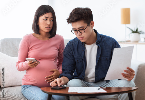 Unhappy Chinese Spouses Calculating Bills Sitting On Sofa At Home