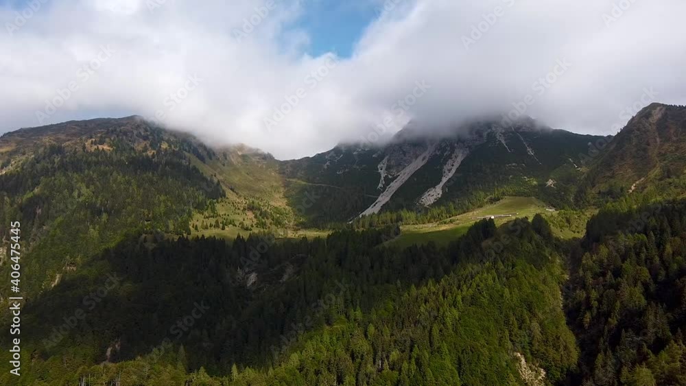 Beautiful panorama shot of mountain formation overgrown with green plants and cloudscape hiding the peak of hills in summer. Slow aerial forward shot.