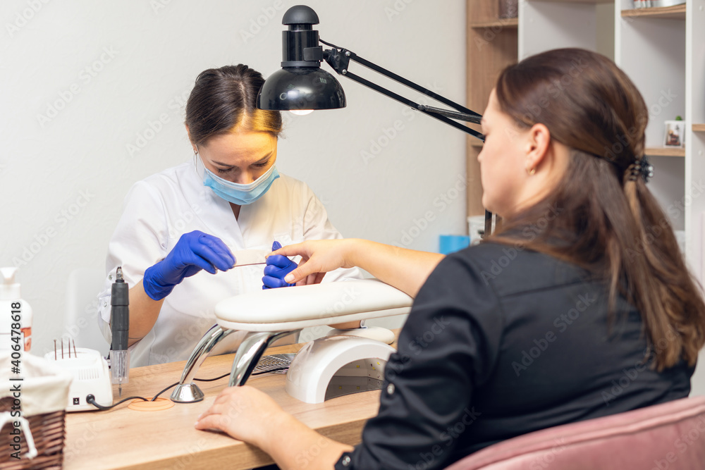 Manicurist doing a manicure in a nail salon using a nail file Manicurist doing a manicure in a nail salon using a nail file
