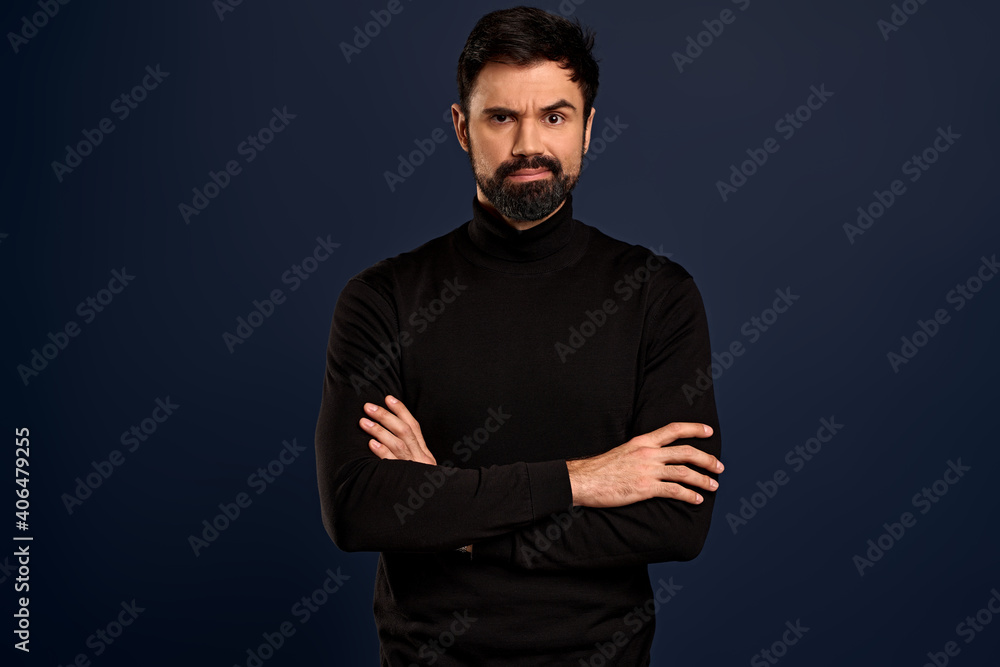 Portrait of serious displeased male stands crossed hands against Blue background, scowl face in dissatisfaction, has quarrel with wife. Discontent man has stubble, expresses annoyannce and negativity Portrait of serious displeased male stands crossed hands against Blue background, scowl face in dissatisfaction, has quarrel with wife. Discontent man has stubble, expresses annoyannce and negativity