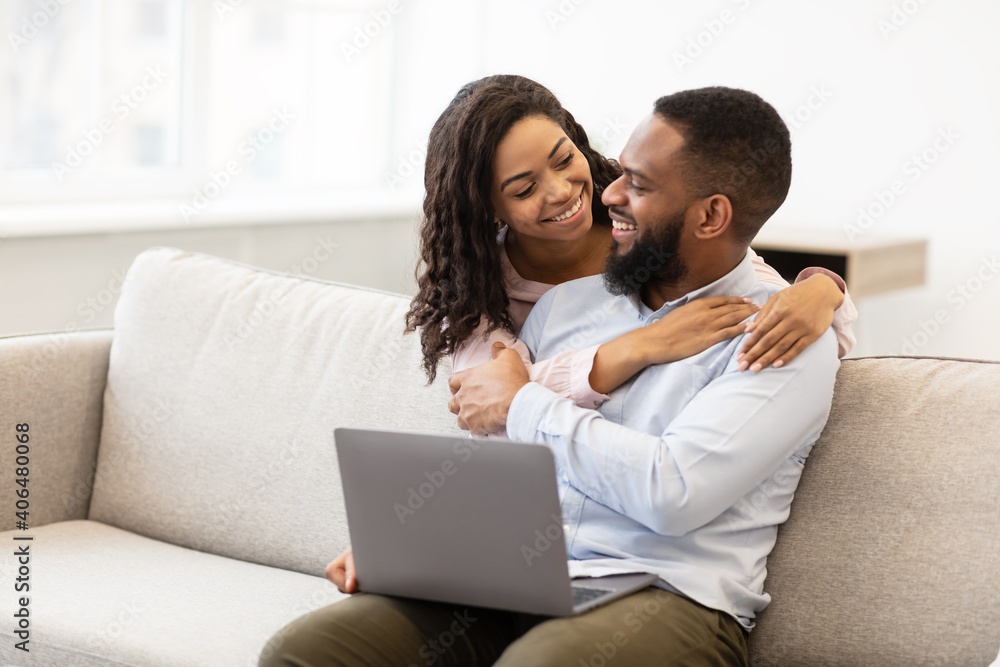 African american couple sitting on couch, using laptop, cuddling African american couple sitting on couch, using laptop, cuddling