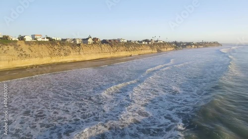 Aerial Drone flies over crashing waves at sunset on beach in San diego, california with clifss in background photo