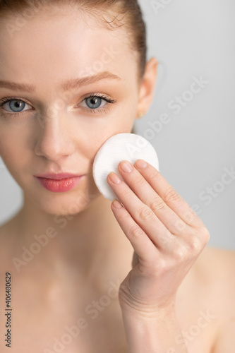Red-Haired Girl Cleansing Skin With Cotton Pad, Gray Background, Vertical