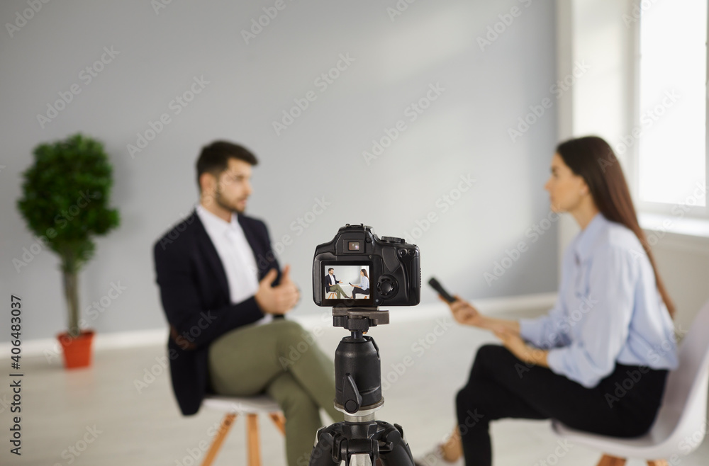 Digital video camera on tripod recording interview with a person in television studio. TV show host talking to celebrity. Journalist or reporter asking famous businessman questions. Blurred background Digital video camera on tripod recording interview with a person in television studio. TV show host talking to celebrity. Journalist or reporter asking famous businessman questions. Blurred background
