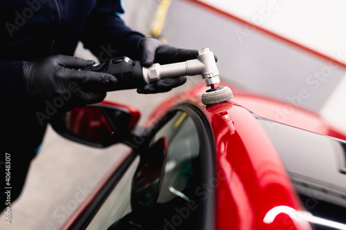 Car detailing - Man with orbital polisher in repair shop polishing car. Selective focus.