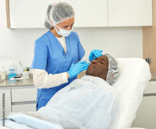 Female doctor examining skin of patient before facial procedure in clinic of esthetic cosmetology