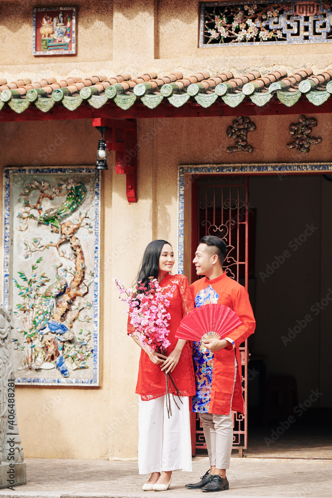 Newlyweds with peach branches and paper fan standing outside the temple after wedding Newlyweds with peach branches and paper fan standing outside the temple after wedding