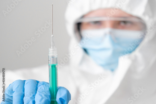 Vaccine in the syringe for prevention of coronavirus in doctor hand, wearing protective mask and protective PPE suit and rubber gloves.