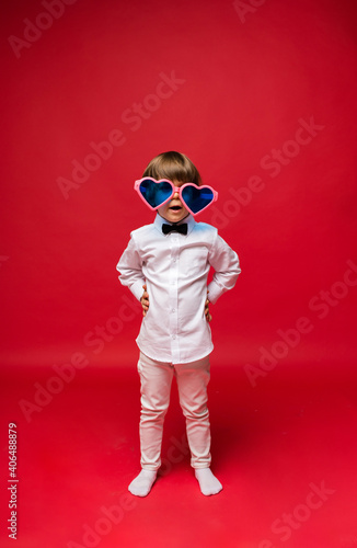 happy boy in big funny heart shaped glasses on red background