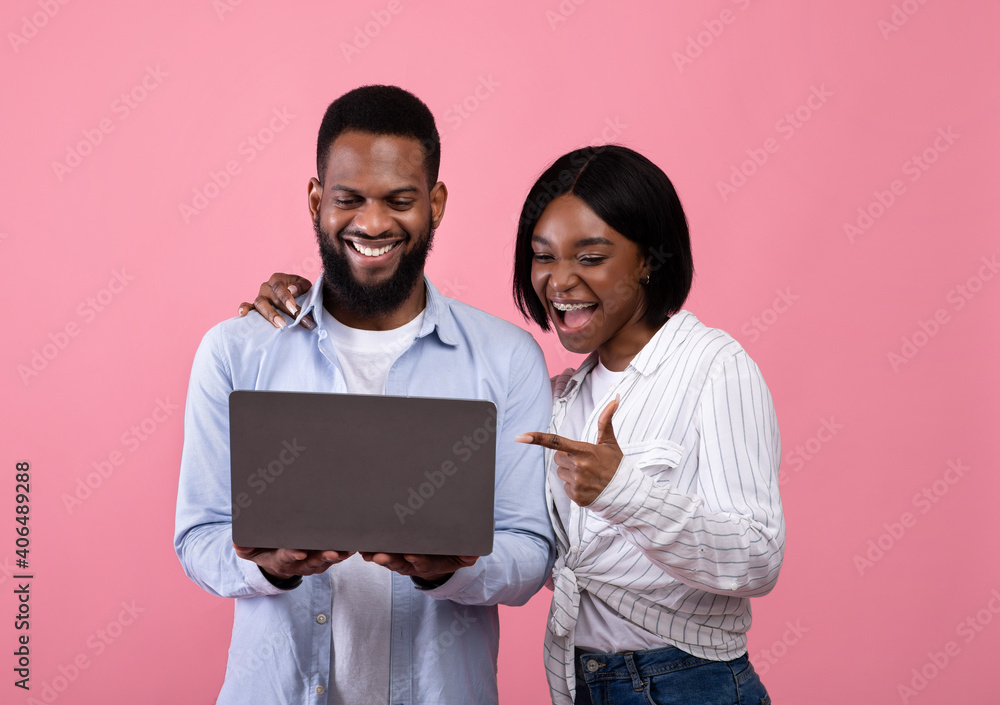 Black couple using laptop, surfing web, watching movie, pointing at screen, learning exciting news on pink background Black couple using laptop, surfing web, watching movie, pointing at screen, learning exciting news on pink background