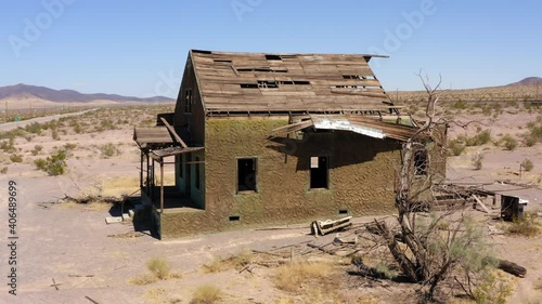Abandoned decrepit run down house sits alone in dry desert area in midday photo