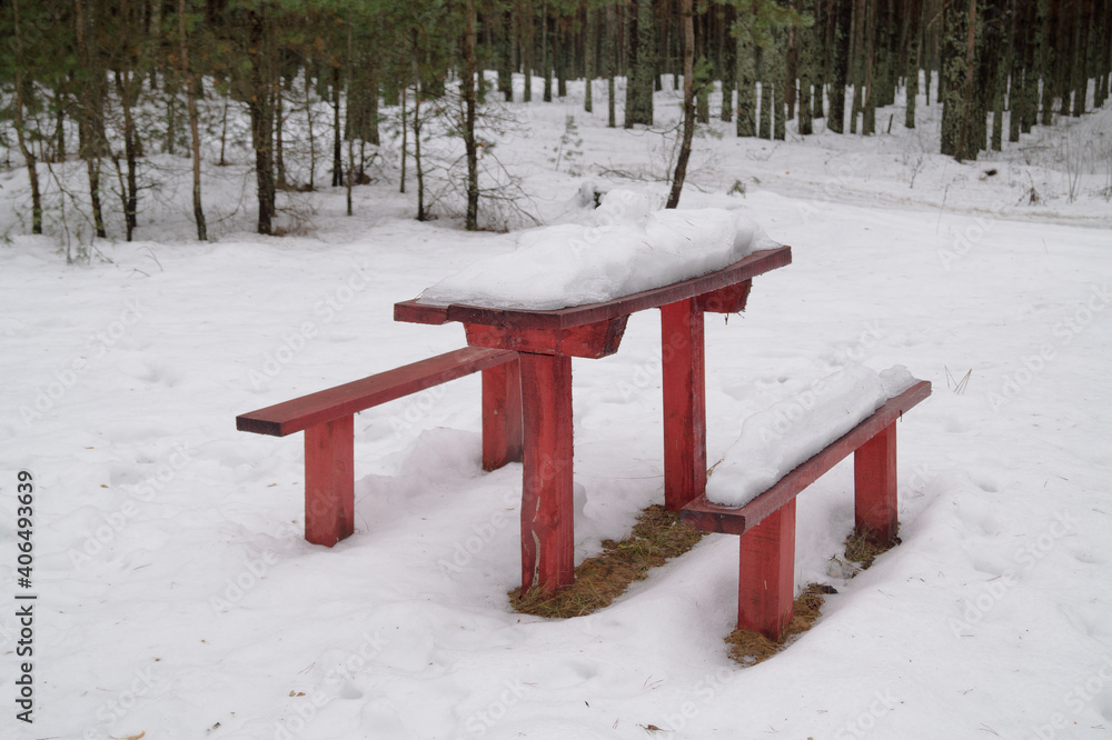 Winter forest, wooden, red table with bench in the snow.
