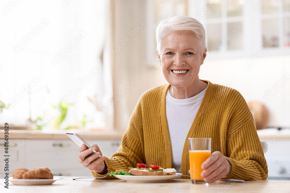 Smiling old lady using mobile phone while having lunch