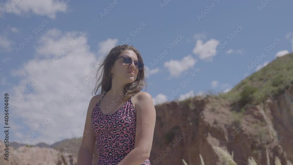 An independent, strong and lonely woman looks up at the mountains with sunglasses, as day turns to night, in the golden hour. She is in a bathing suit. She admires nature and thinks about the future. An independent, strong and lonely woman looks up at the mountains with sunglasses, as day turns to night, in the golden hour. She is in a bathing suit. She admires nature and thinks about the future.