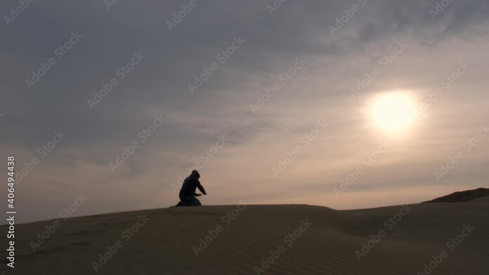 Wide shot of a man lost in the desert, kneeling and praying to be found. Wide shot of a man lost in the desert, kneeling and praying to be found.