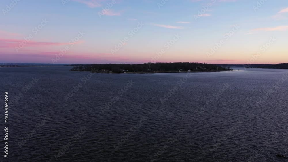 an aerial shot over a bay focused on an island during a beautiful sunrise. It is golden hour and the sky is pink and blue with a few clouds. The camera is stationary as the waves moves to the right. an aerial shot over a bay focused on an island during a beautiful sunrise. It is golden hour and the sky is pink and blue with a few clouds. The camera is stationary as the waves moves to the right.