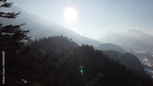 between the trees towards the foggy sun, in the snow-covered bernese alps (drone view) photo