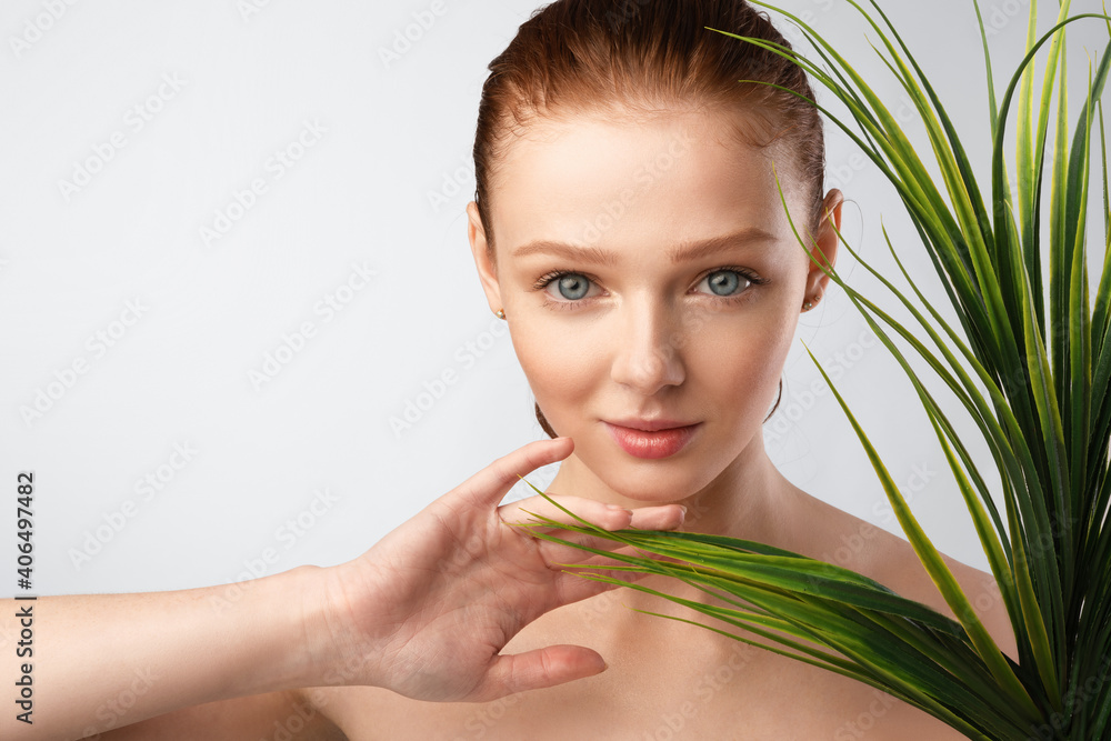 Naklejka premium Ginger-Haired Young Lady Posing Touching Green Plant On Gray Background