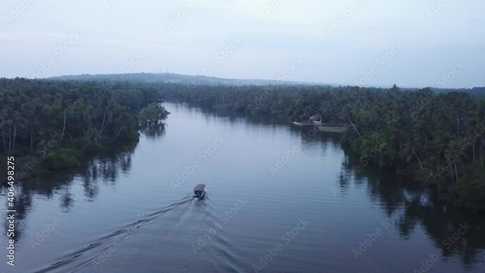 Boat Cruising In Rippled Backwaters Of Poovar With Lush Green Vegetation And Coconut Trees Lined Up On The Shores In Kerala, India - aerial drone shot Boat Cruising In Rippled Backwaters Of Poovar With Lush Green Vegetation And Coconut Trees Lined Up On The Shores In Kerala, India - aerial drone shot