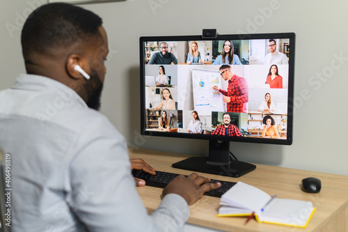 Brainstorm, online video meeting, virtual conference with multi ethnic coworkers, employee, colleagues. View over shoulder of an African guy on a screen with webcam shots of diverse people