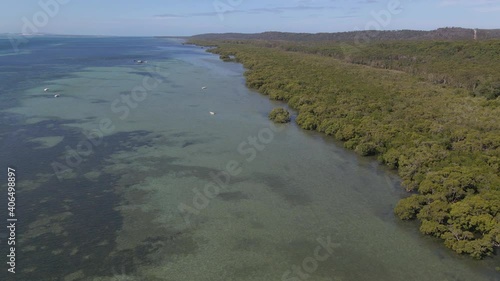 Boats Floating On Calm Water Of Coral Sea With Lush Green Forest - North Stradbroke Island, Minjerribah, Queensland, Australia. - aerial photo