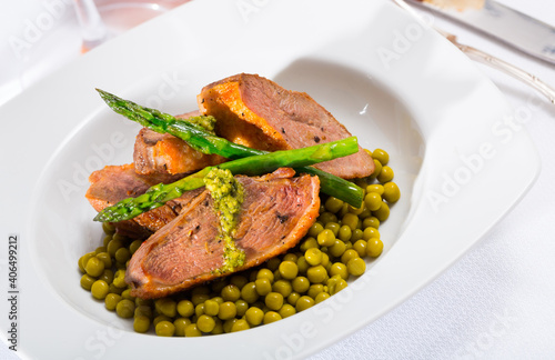 Tasty grilled duck fillet served with green peas, asparagus and pesto sauce