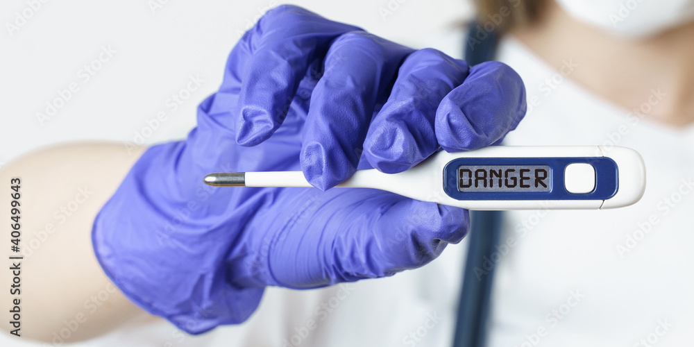 The doctor holds a thermometer in his hands, on the electronic screen of which it is written - DANGER The doctor holds a thermometer in his hands, on the electronic screen of which it is written - DANGER