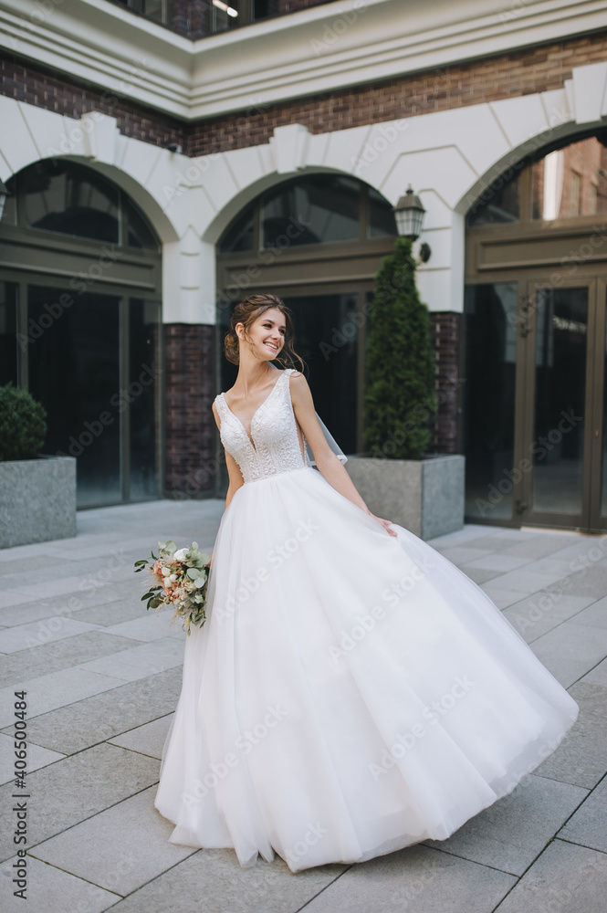 A beautiful curly-haired bride in a white dress, a long veil with a bouquet in her hands is spinning and dancing on the background of buildings in the city on the boulevard. Wedding portrait. A beautiful curly-haired bride in a white dress, a long veil with a bouquet in her hands is spinning and dancing on the background of buildings in the city on the boulevard. Wedding portrait.