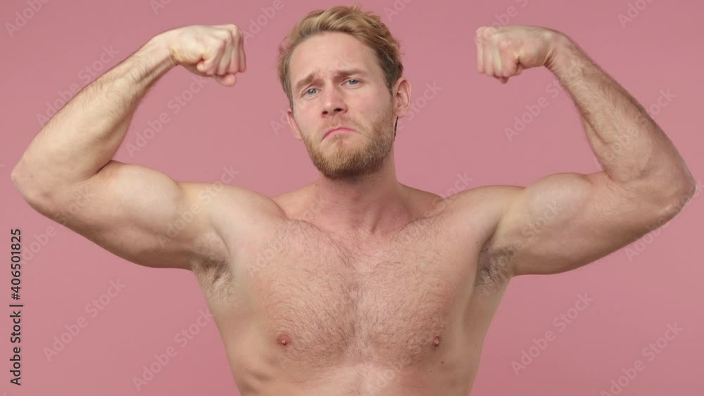 Smiling cheerful strong sporty bearded naked young man 20s years old perfect skin isolated on pink background studio. Skin care healthcare cosmetic procedures concept. Showing biceps mucles on hands Smiling cheerful strong sporty bearded naked young man 20s years old perfect skin isolated on pink background studio. Skin care healthcare cosmetic procedures concept. Showing biceps mucles on hands