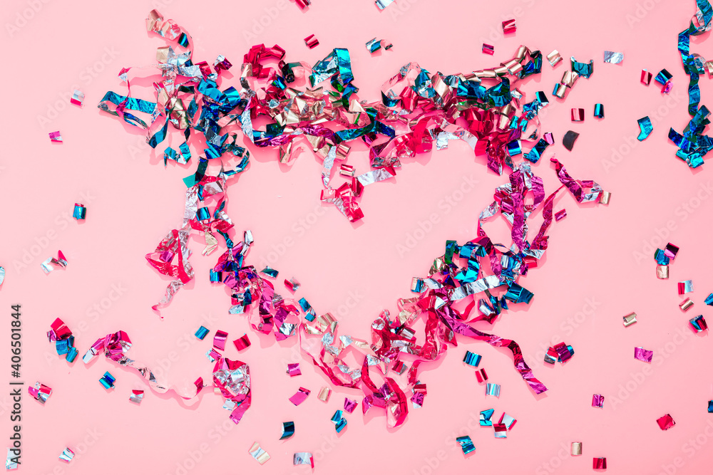Colorful bright confetti and streamers in form of heart on pink background,  top view. Copy space