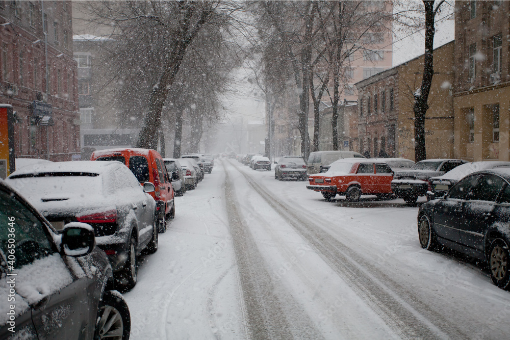 Cars are parked in the city on a snowy street in winter. Snowing. Cars are parked in the city on a snowy street in winter. Snowing.