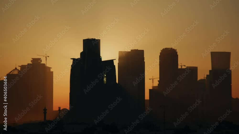 West Bay skyline in Doha, Qatar being silhouetted during sunrise and sun peaking out from behind the towers. West Bay skyline in Doha, Qatar being silhouetted during sunrise and sun peaking out from behind the towers.