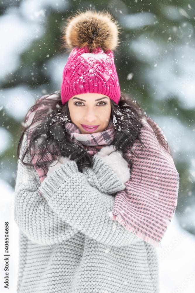 Winter fashion outdoors captured on a female model wearing ping pom pom hat, grey sweater and pink knitted scarf.