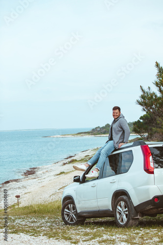 man sitting on the car roof enjoying view of summer sea
