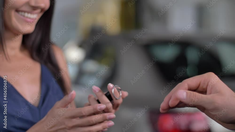 Close-up of dealer's hand giving keys from purchased car to smiling female customer in auto showroom. New car owner and salesman sealing deal with handshake during buying new automobile at dealership Close-up of dealer's hand giving keys from purchased car to smiling female customer in auto showroom. New car owner and salesman sealing deal with handshake during buying new automobile at dealership
