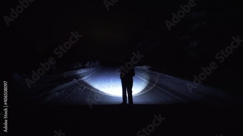 A girl walks alone in the winter through the forest at night, with a flashlight