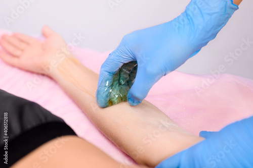 The work of a beautician in a beauty salon. The beautician prepares for depilation and applies sugar paste to the woman's hand. Focus on hand and wax.