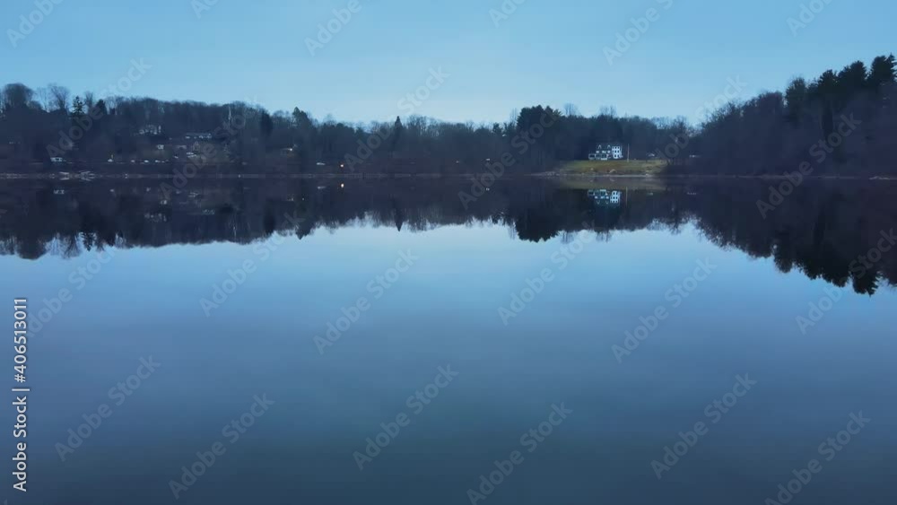 Drone flying just above the water of a calm lake with a glassy surface and then rising in the air to show a small town and mountains after sunset, during blue hour in america Drone flying just above the water of a calm lake with a glassy surface and then rising in the air to show a small town and mountains after sunset, during blue hour in america