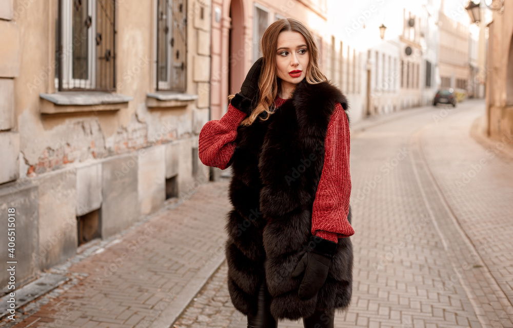 Fototapeta premium Outdoor photo of fashionable female model walking around city in winter vacation. Fashionable girl walking on Warsaw street in Old Town. Poland.