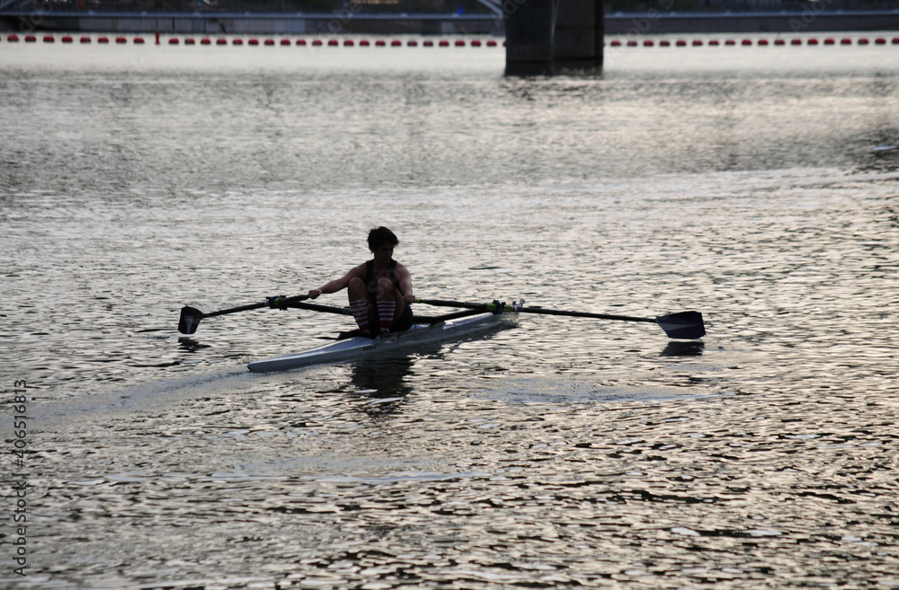 Sunlight reflects off the surface of a lake, silhouetting a young person kayaking as he paddles along Sunlight reflects off the surface of a lake, silhouetting a young person kayaking as he paddles along