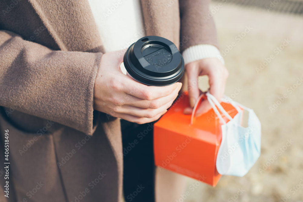 Close up of woman hands holding take away food and cup of coffee. Drinking hot beverage outdoors on the street. Selective focus, natural light