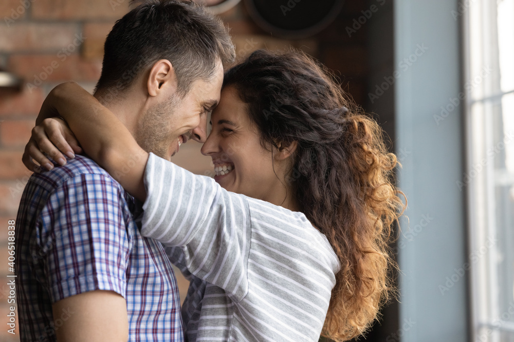 Happy young Caucasian couple renters hug embrace look in eyes relax on romantic weekend in new home. Smiling millennial man and woman embrace enjoy tender sweet time in own house. Relations concept.