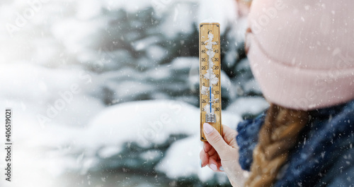 Photos A young adult woman hold in her hand snowy thermometer showing a temperature slightly below freezing