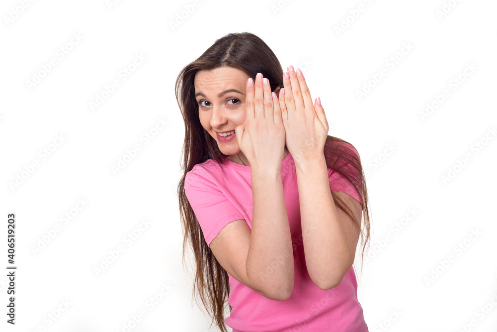 Cheerful woman looks out from behind her hands, isolated on white background. Female brunette in a pink sweater. Place for text. Cheerful woman looks out from behind her hands, isolated on white background. Female brunette in a pink sweater. Place for text.